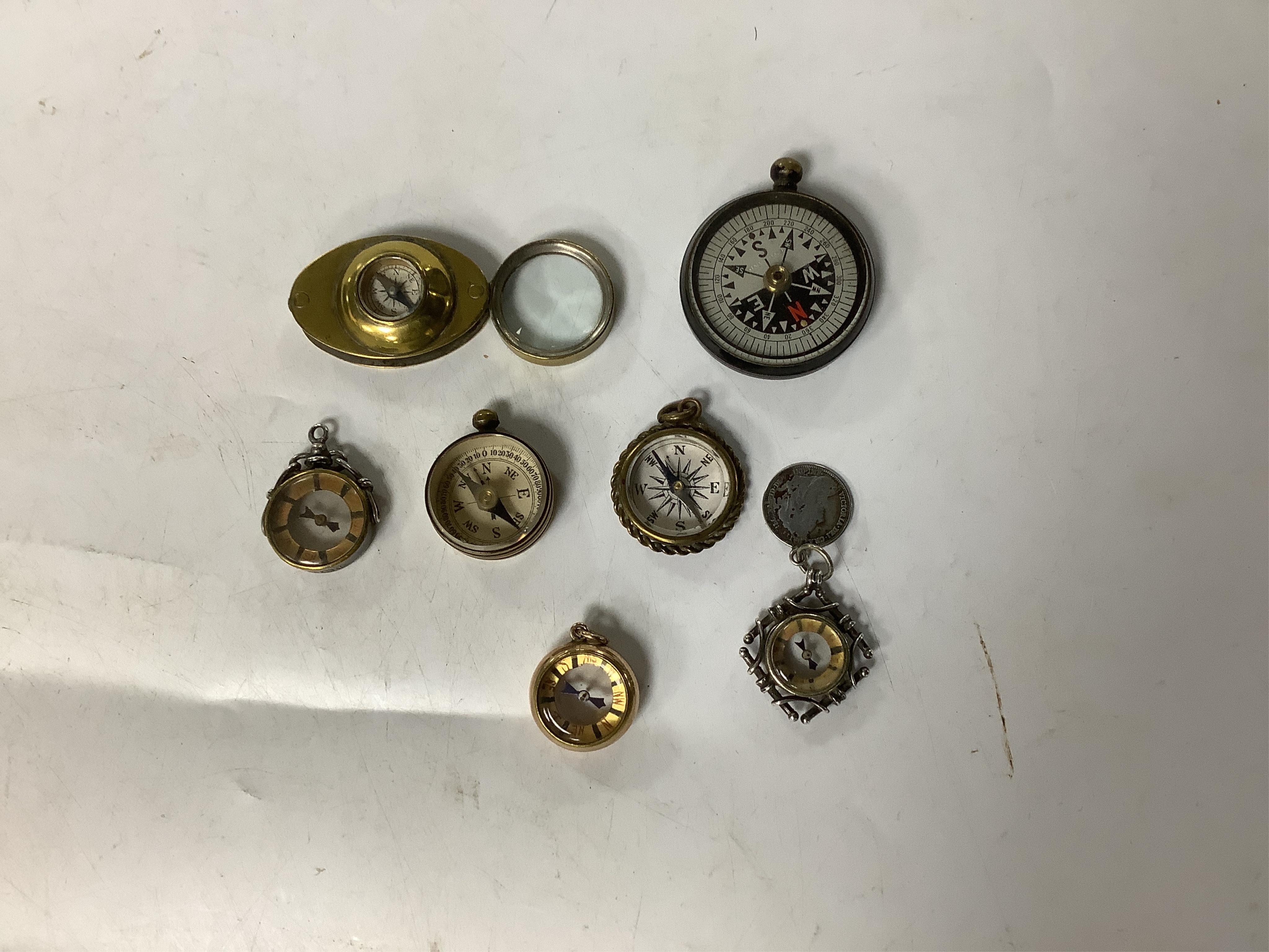 A late Victorian 9ct mounted compass fob, hallmarked for Birmingham, 1900, together with an Edwardian silver mounted compass fob and five other base metal mounted compasses including a combination compass and loupe, 35mm